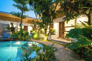 A pool area with a curved edge, surrounded by lush greenery and potted plants. - Lakubumi Pavilion (Ungasan)