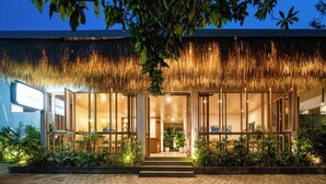 A modern building with a thatched roof entrance, glass doors, and a well-lit interior visible through the doors. - Lakubumi Pavilion (Ungasan)
