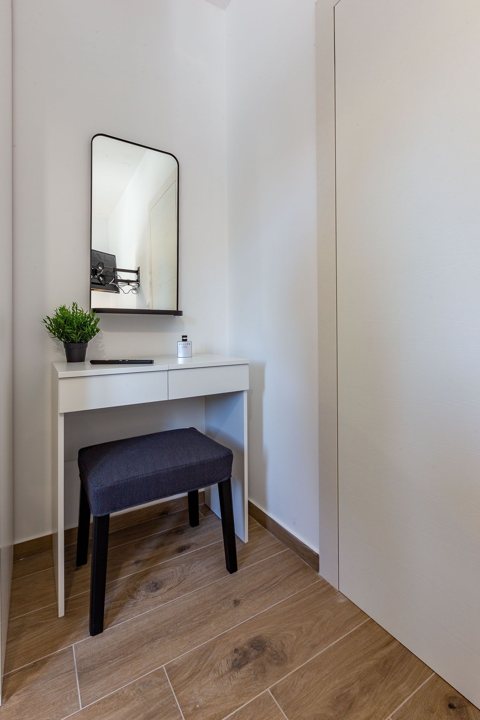 A white desk with a mirror, a small potted plant, and a bench.