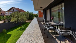 En moderne udendørs terrasse med et langt bord og stole, et lille haveområde og udsigt til nabohuse.
