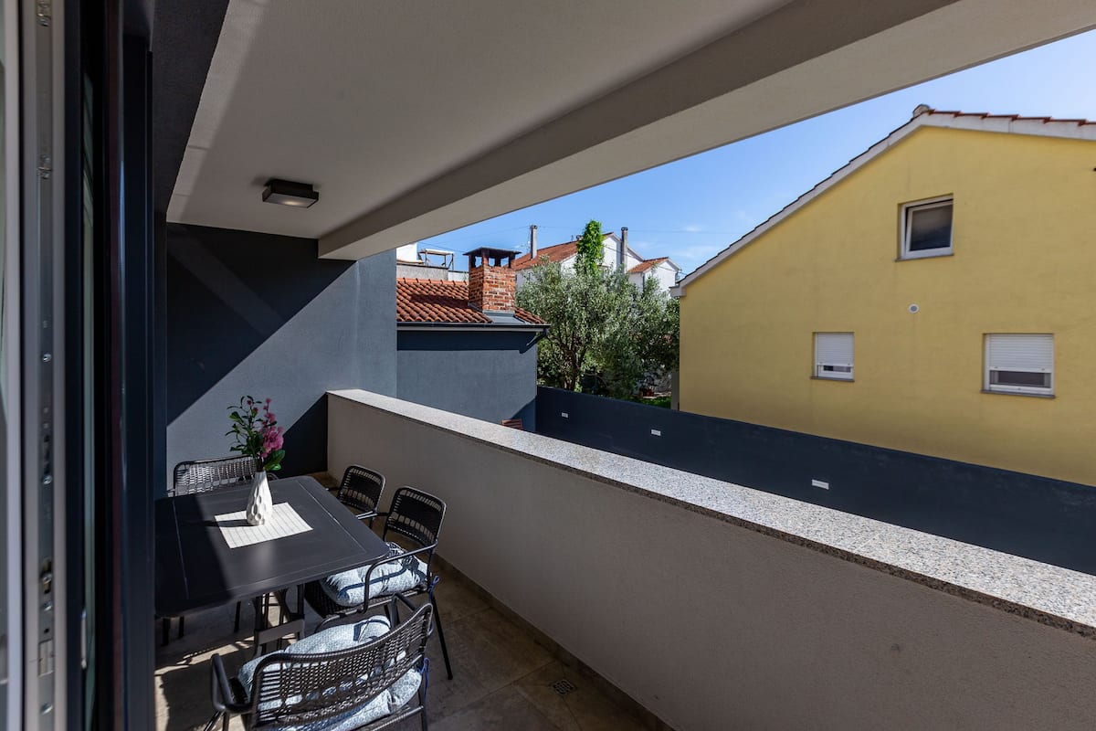 A balcony with a table and chairs, a potted plant, and a view of neighboring buildings.