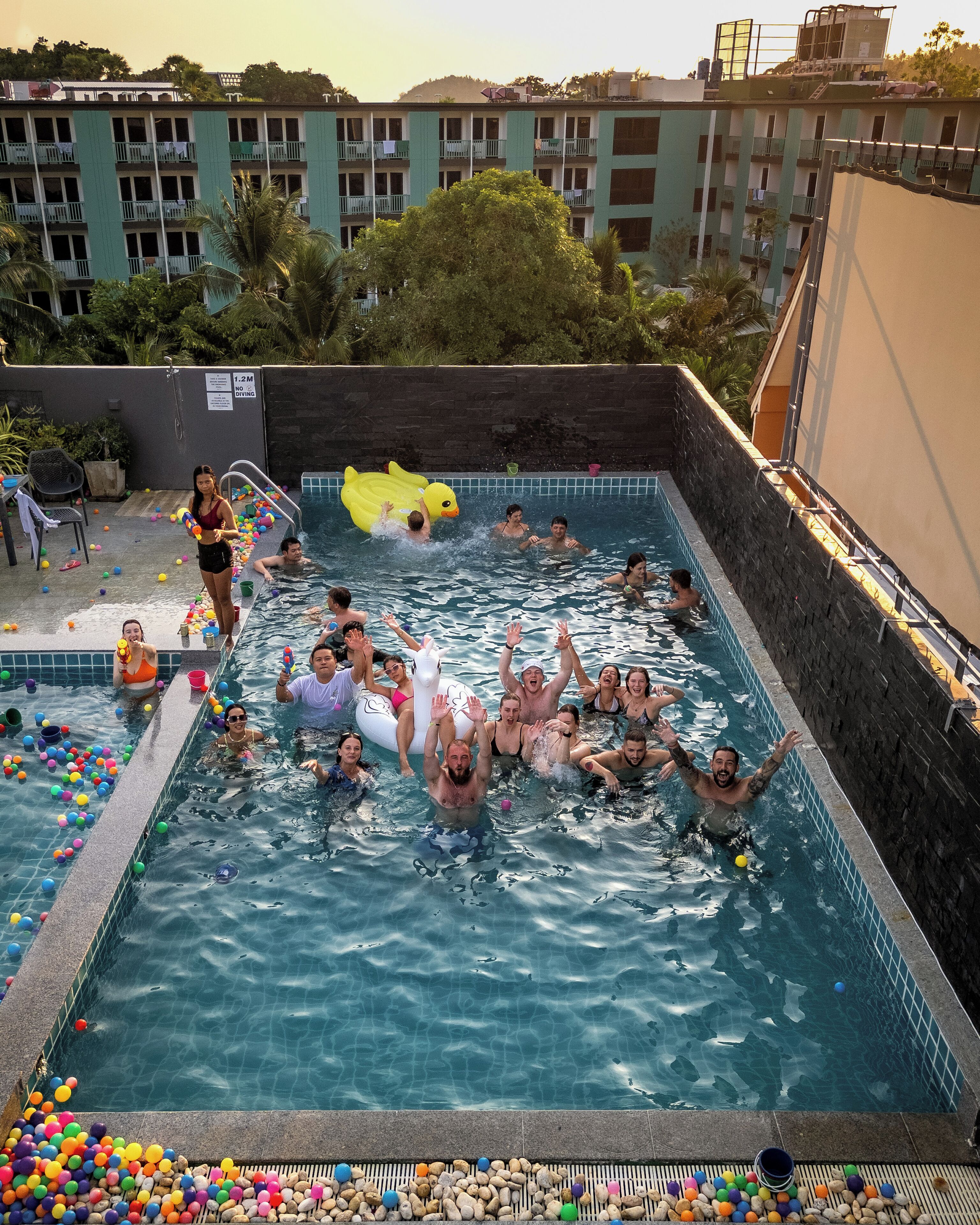 En swimmingpool med mennesker, der nyder vandet, omgivet af en stenvæg og en bygning i baggrunden.