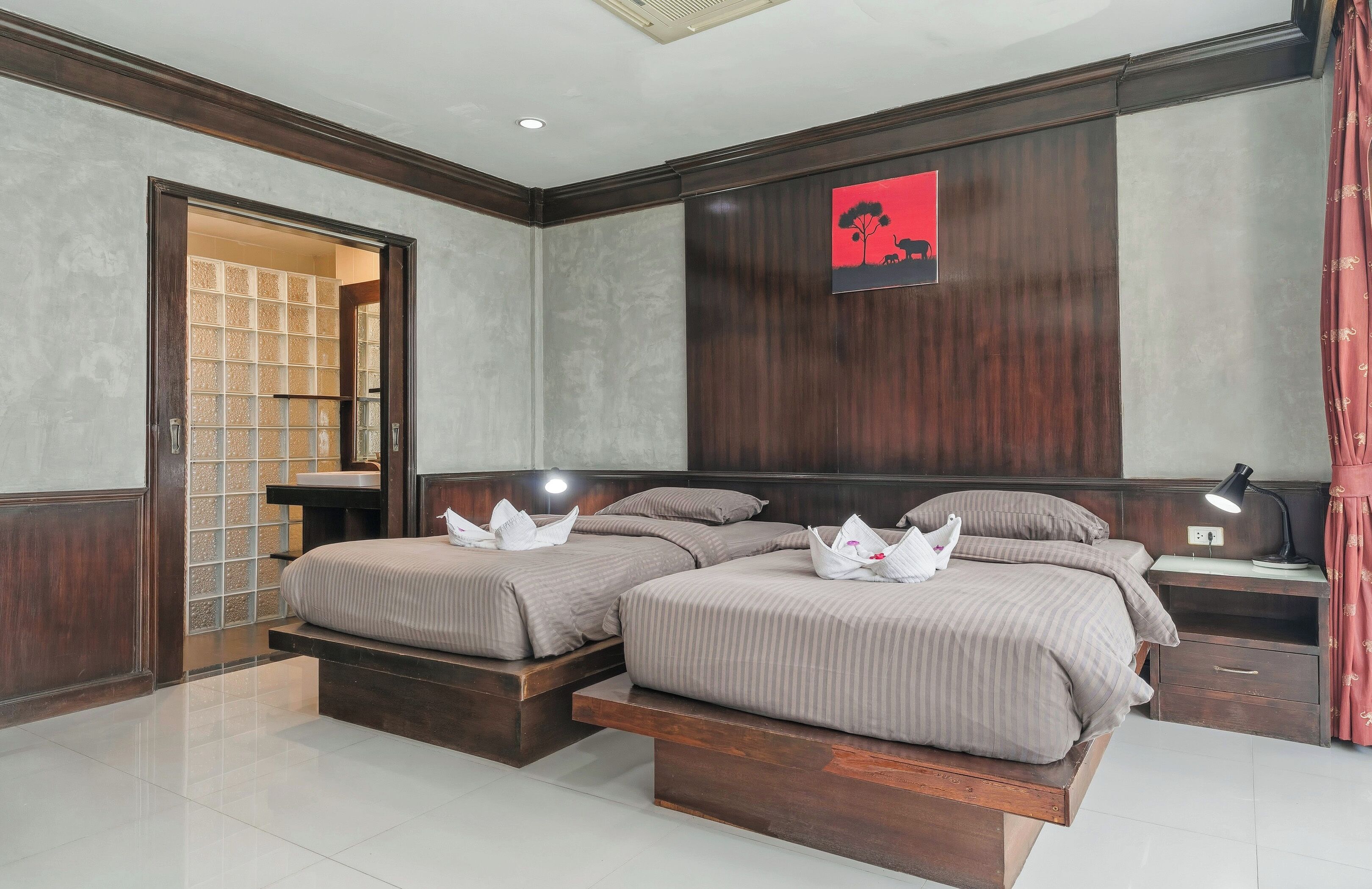 A hotel room with two beds, a desk, a nightstand, a lamp, and a red curtain.