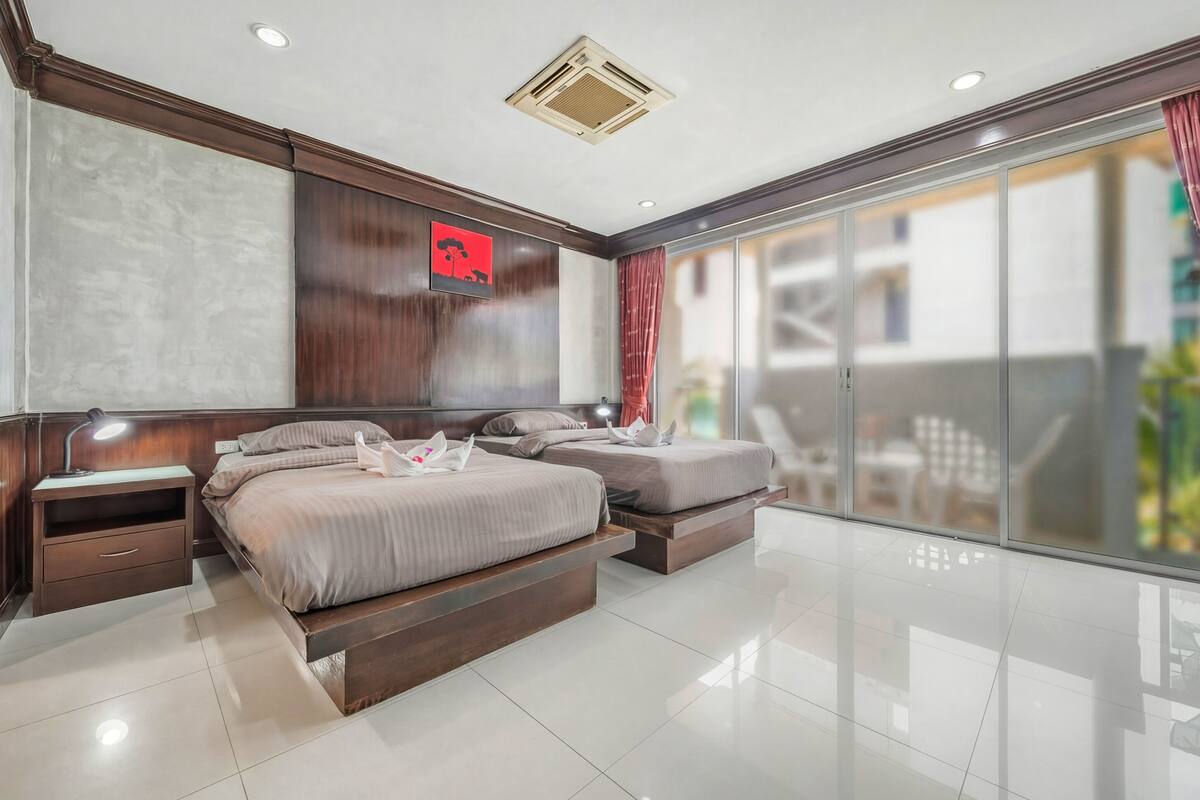 A modern bedroom with a large bed, bedside tables, a TV, and a sliding glass door to a balcony.