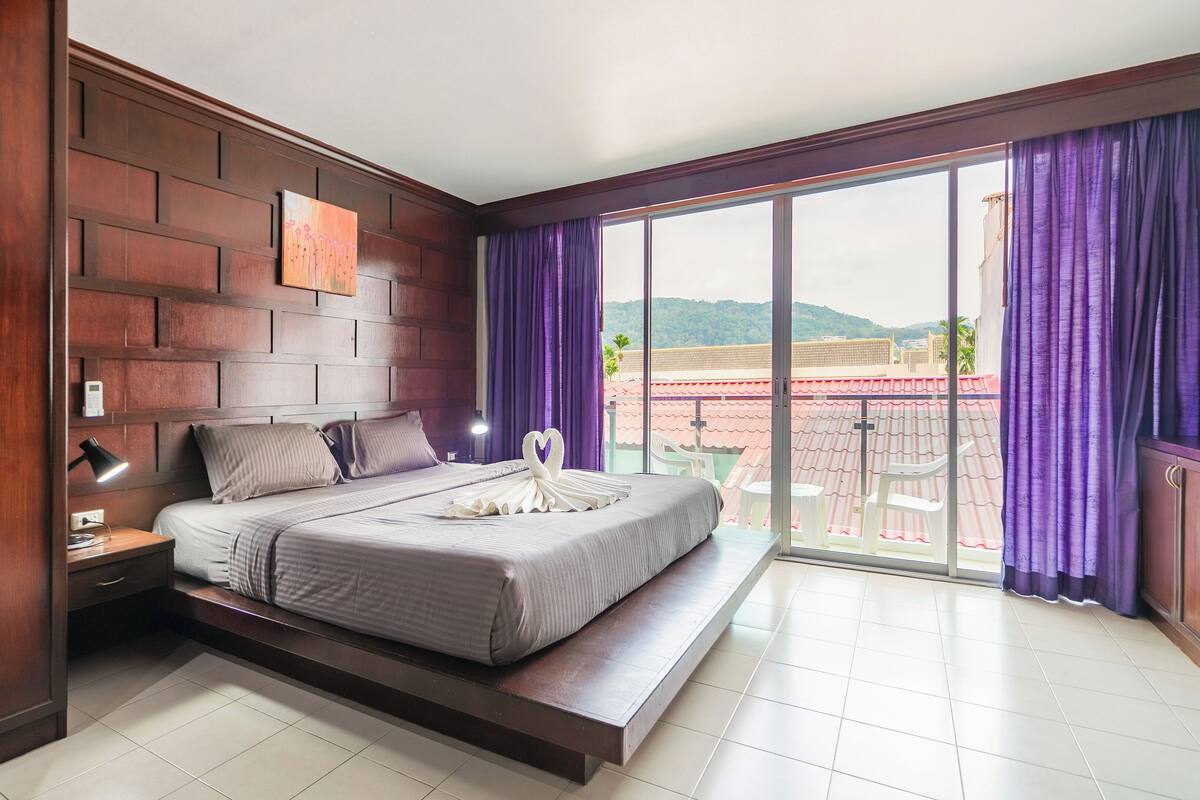 A modern hotel room with a large bed, a nightstand, a desk, and a view of the outside balcony.
