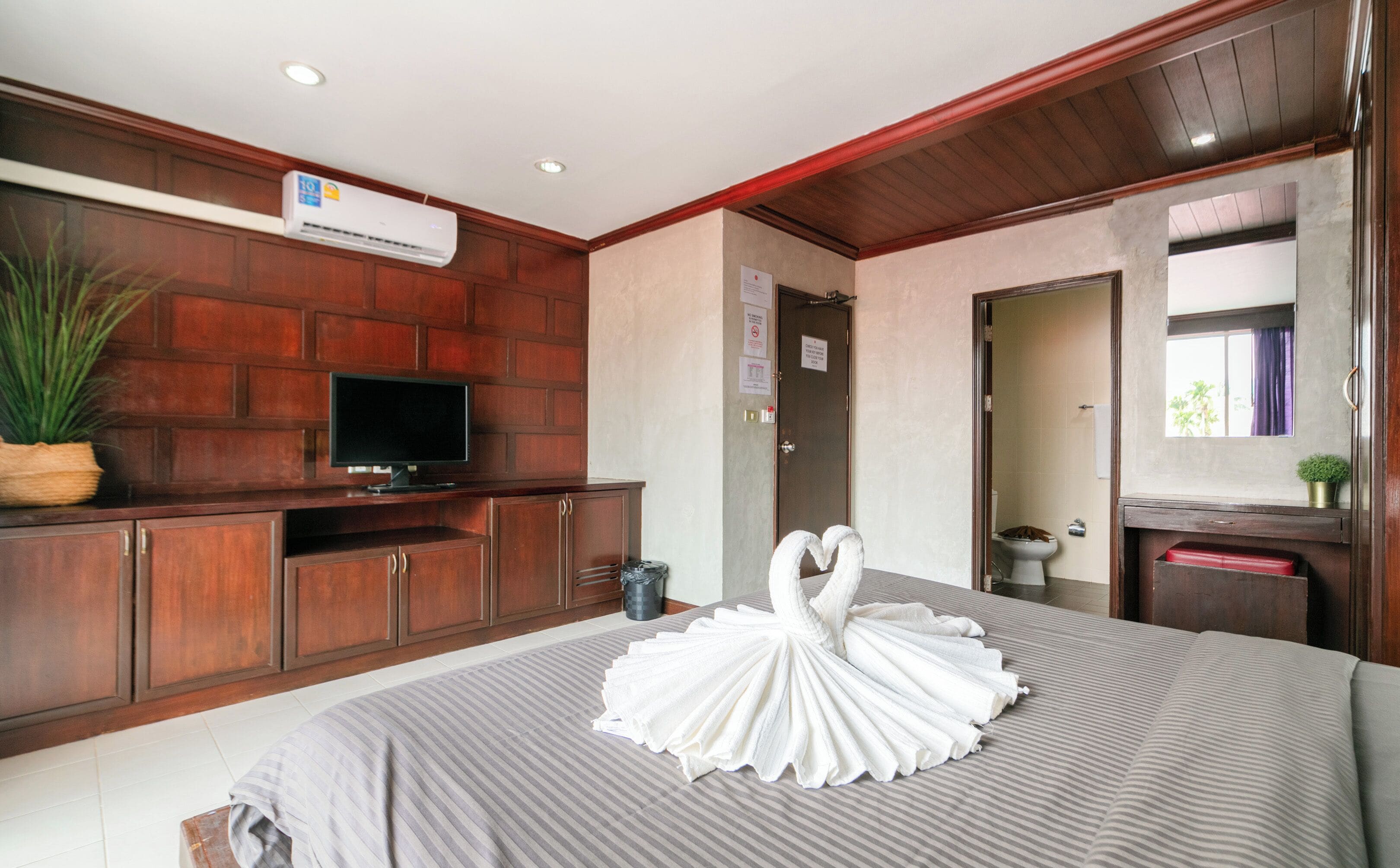 A hotel room with a large bed, a flat-screen TV, a potted plant, and a wooden cabinet.