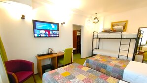 Une chambre avec des lits superposés, un bureau avec une chaise, une télévision et un lit recouvert d’une couverture aux couleurs vives.