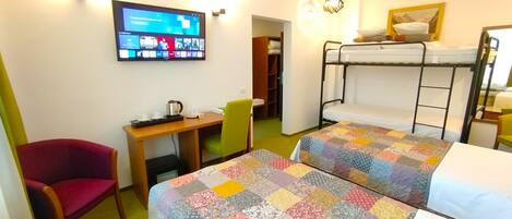 Ein Zimmer mit Etagenbetten, einem Schreibtisch mit Stuhl, einem Fernseher und einem Bett mit bunter Bettdecke.
