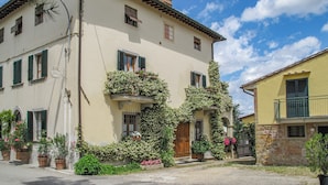 A two-story building with a balcony, a wooden door, and a window with shutters. - Francigena Loggia Apartment Shared Pool (Gambassi Terme)