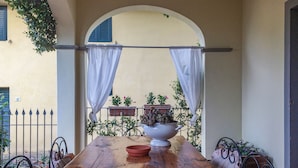 A wooden table with a white bowl and a white pot, surrounded by metal chairs with white cushions. - Francigena Loggia Apartment Shared Pool (Gambassi Terme)