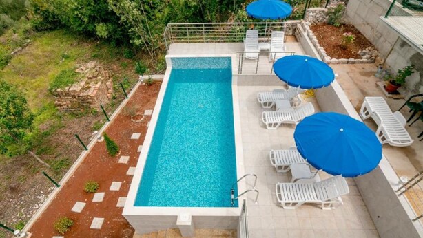 A rectangular swimming pool with a white border, surrounded by white lounge chairs and blue umbrellas. - Tranquil Retreat With Private Pool in Lustica Bay (Klinci)