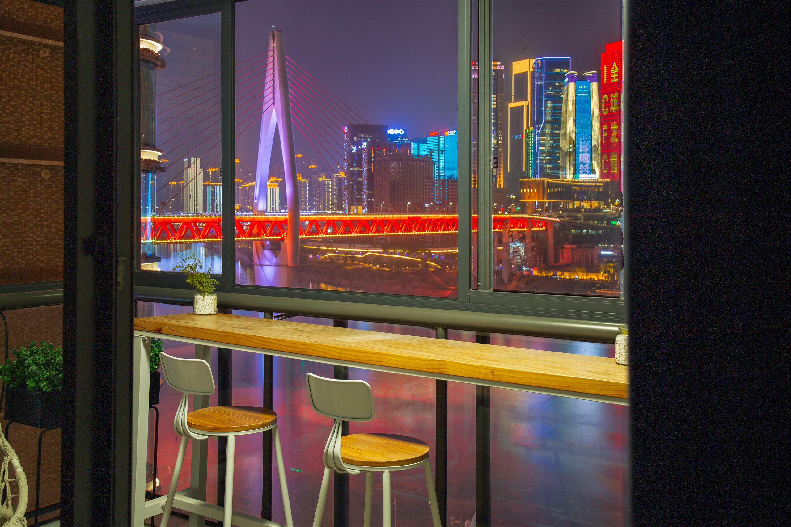 Un bar con due sgabelli e vista sulla città di notte, con un ponte e edifici illuminati.