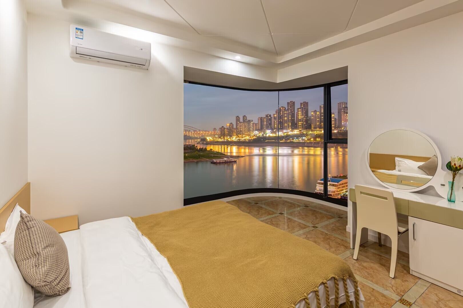 A hotel room with a bed, a desk, a chair, a mirror, and a large window with a cityscape view.