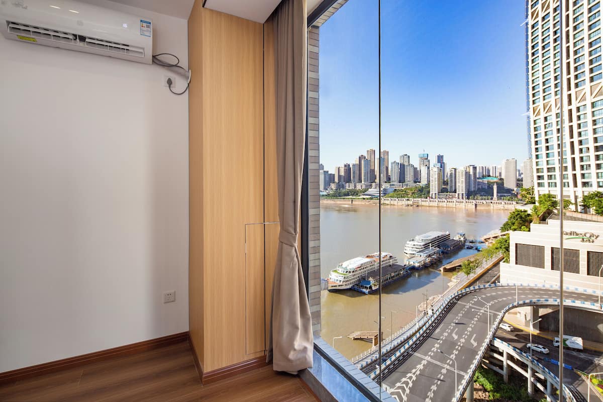 A room with a large window overlooking a river with boats and a city skyline.