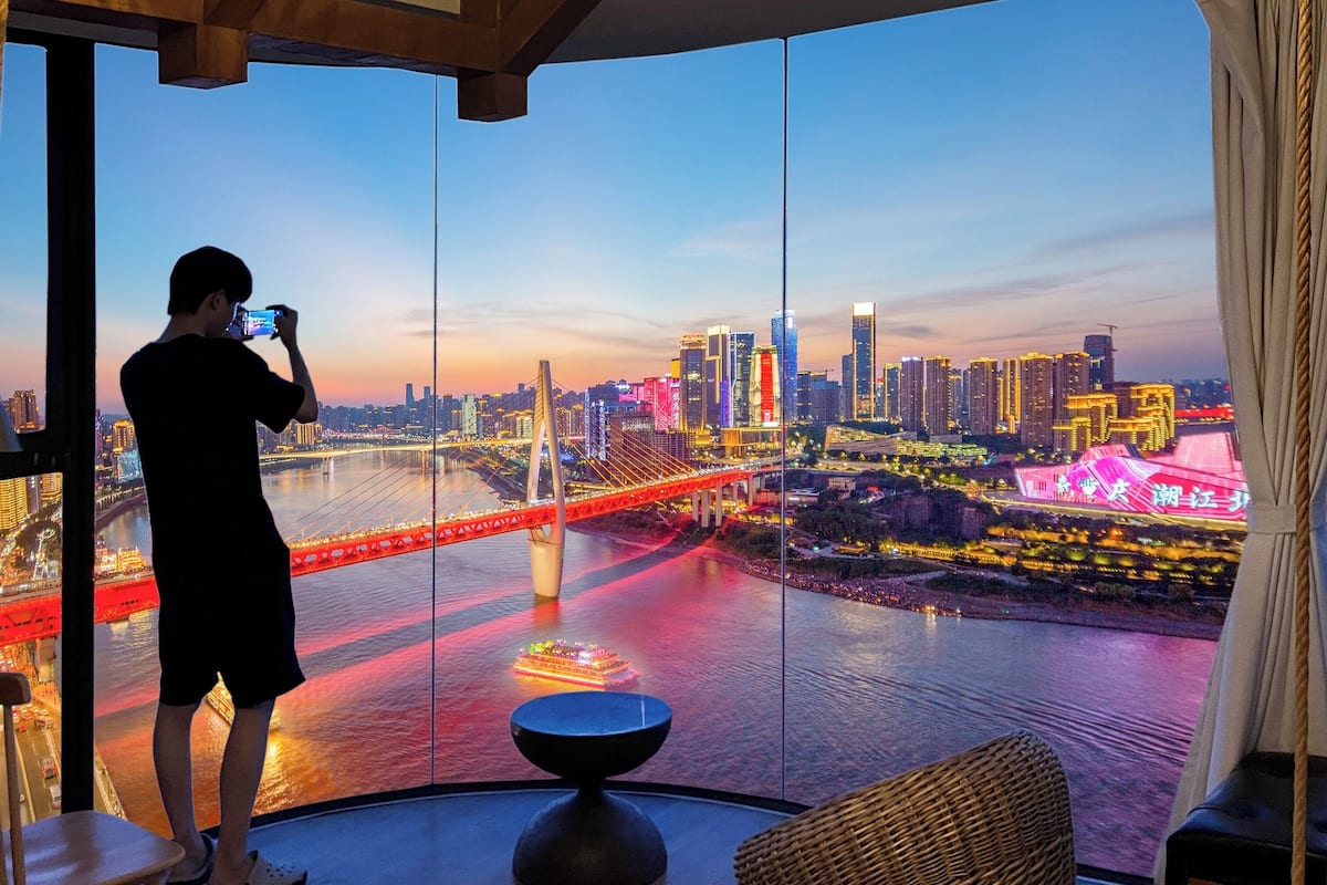 A person taking a photo of a cityscape with a bridge and buildings.