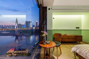 Habitación de hotel con un ventanal grande que ofrece vistas a un horizonte urbano y un río.