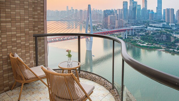 A balcony with wicker chairs and a small table, overlooking a cityscape with a prominent bridge and high-rise buildings. -  Nuanyu Apartment with River View & Drone Show View (Chongqing)