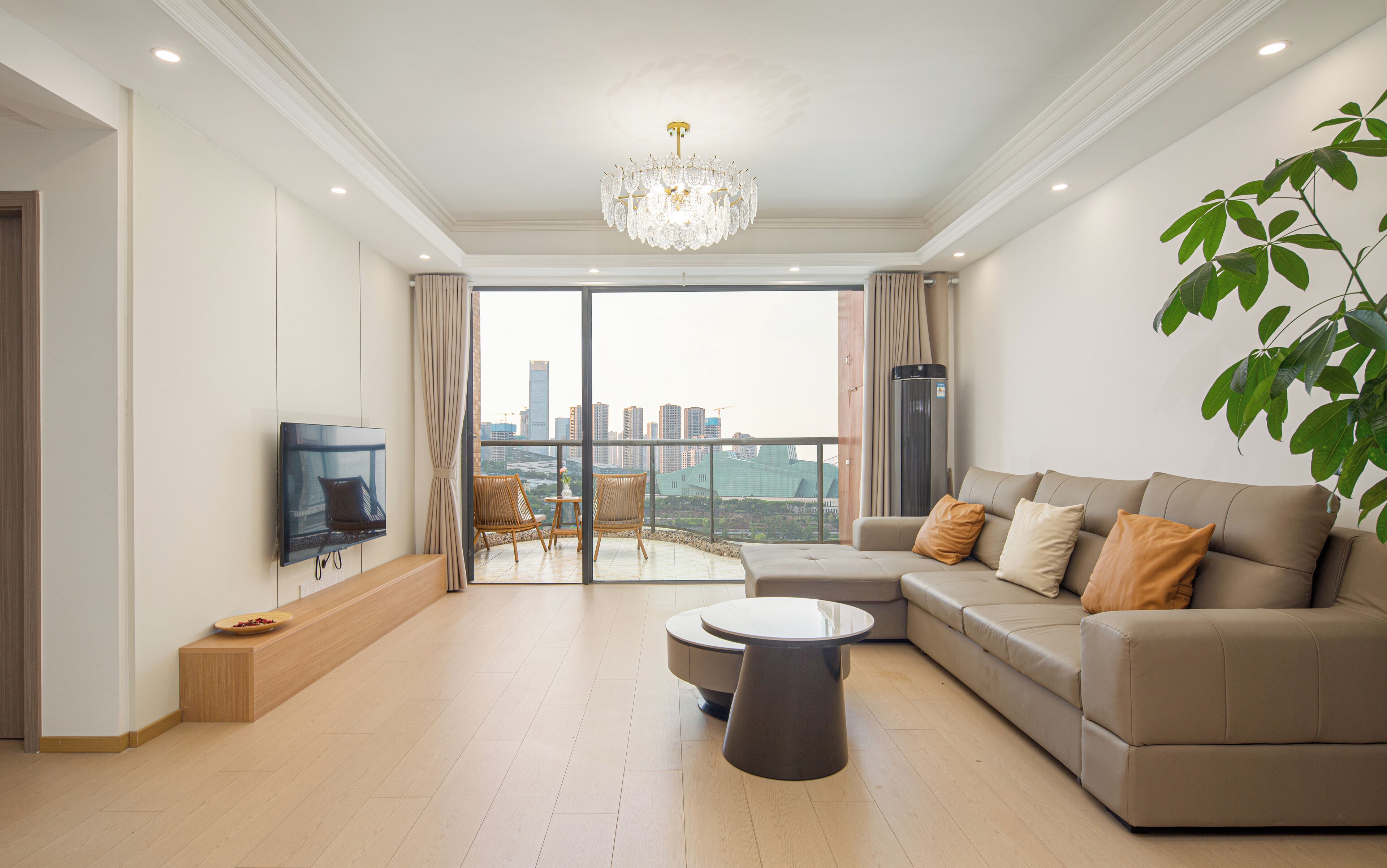 A modern living room with a sofa, a TV, a chandelier, and a balcony with a city view.