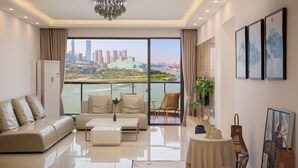 A modern living room with a sofa, coffee table, and a view of a cityscape through large windows. -  Nuanyu Apartment with River View & Drone Show View (Chongqing)