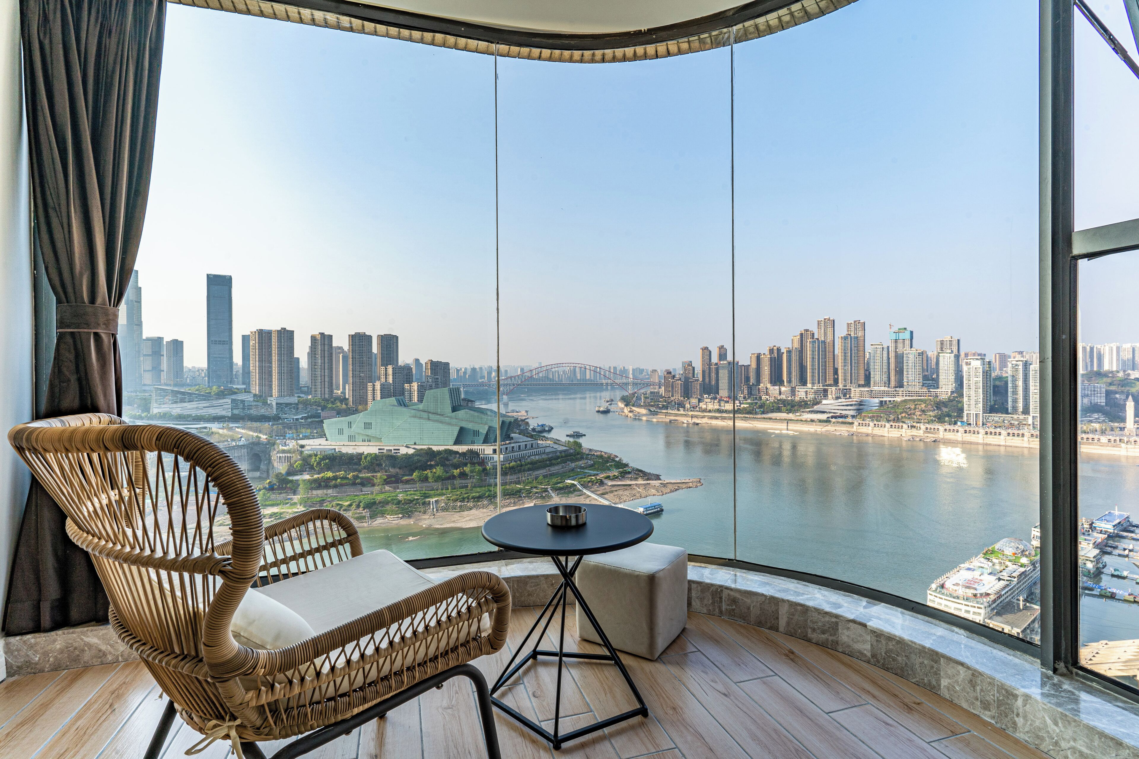 A high-rise room with a panoramic view of a city skyline and a river.