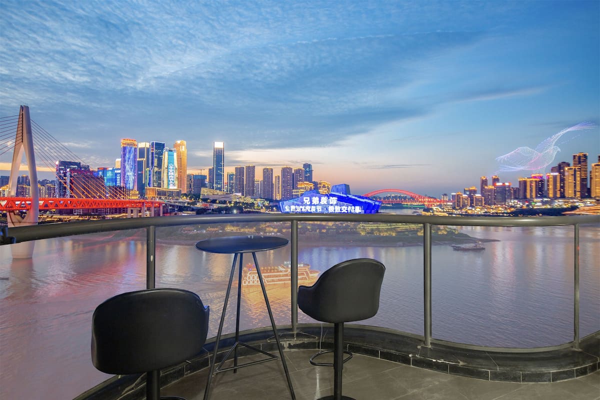 A view from a balcony with two chairs, a city skyline, a bridge, and a river.