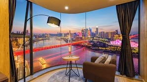 A room with a large curved window, a sofa, a small round table, and a lamp. -  Nuanyu Apartment with River View & Drone Show View (Chongqing)
