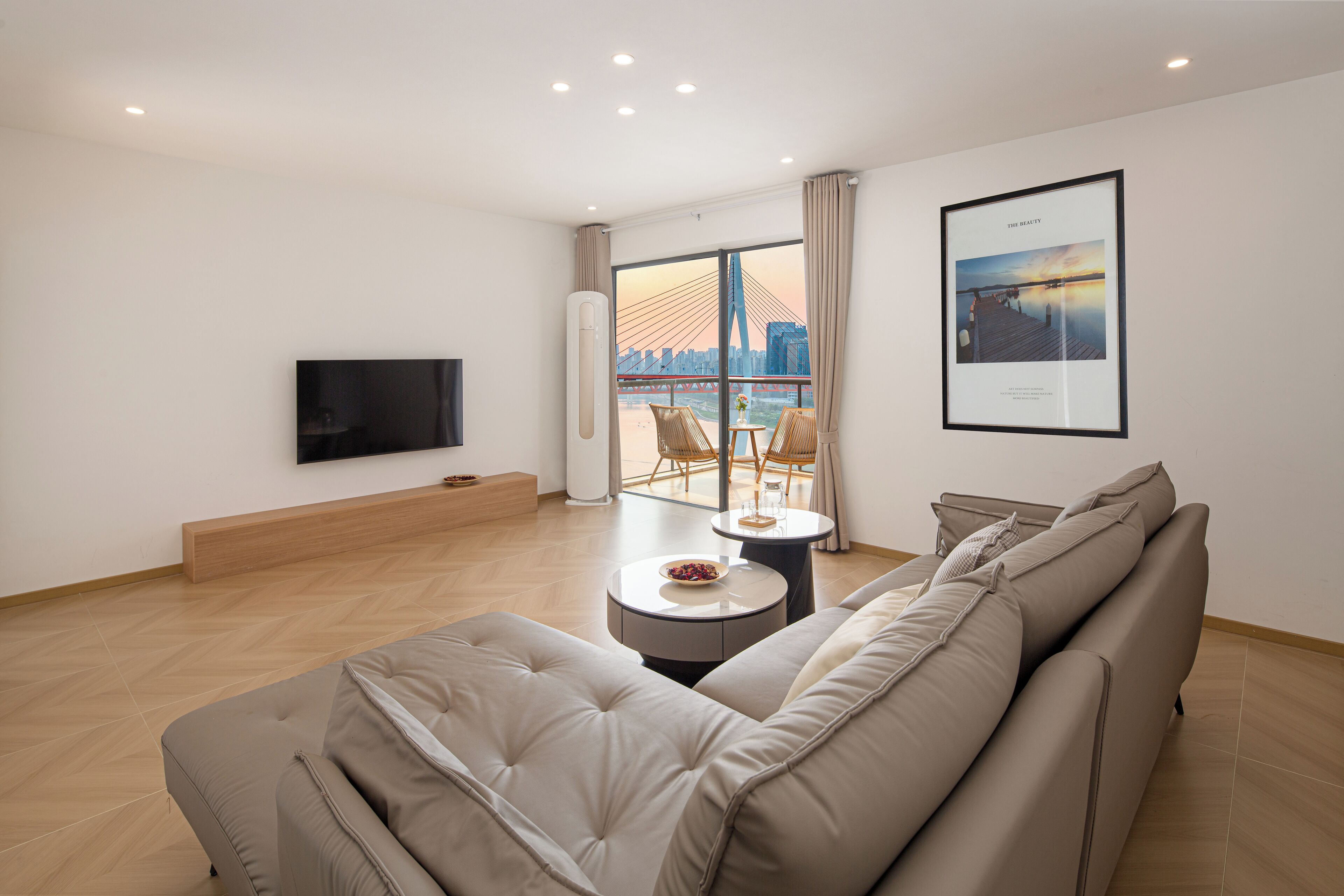 A modern living room with a large sofa, a flat-screen TV, a dining table with chairs, and a large window with a city view.