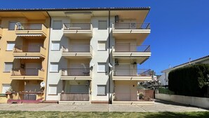 A multi-story residential building with balconies, a parking area, and a well-maintained lawn.