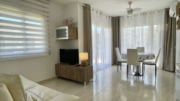 A modern living room with a flat-screen TV, a lamp, and a dining area with a table and chairs.