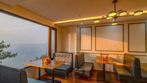 A modern interior with a large window offering a mountain view, a wooden table, and two seating areas with cushioned benches. - Shimla Inn (Shimla)