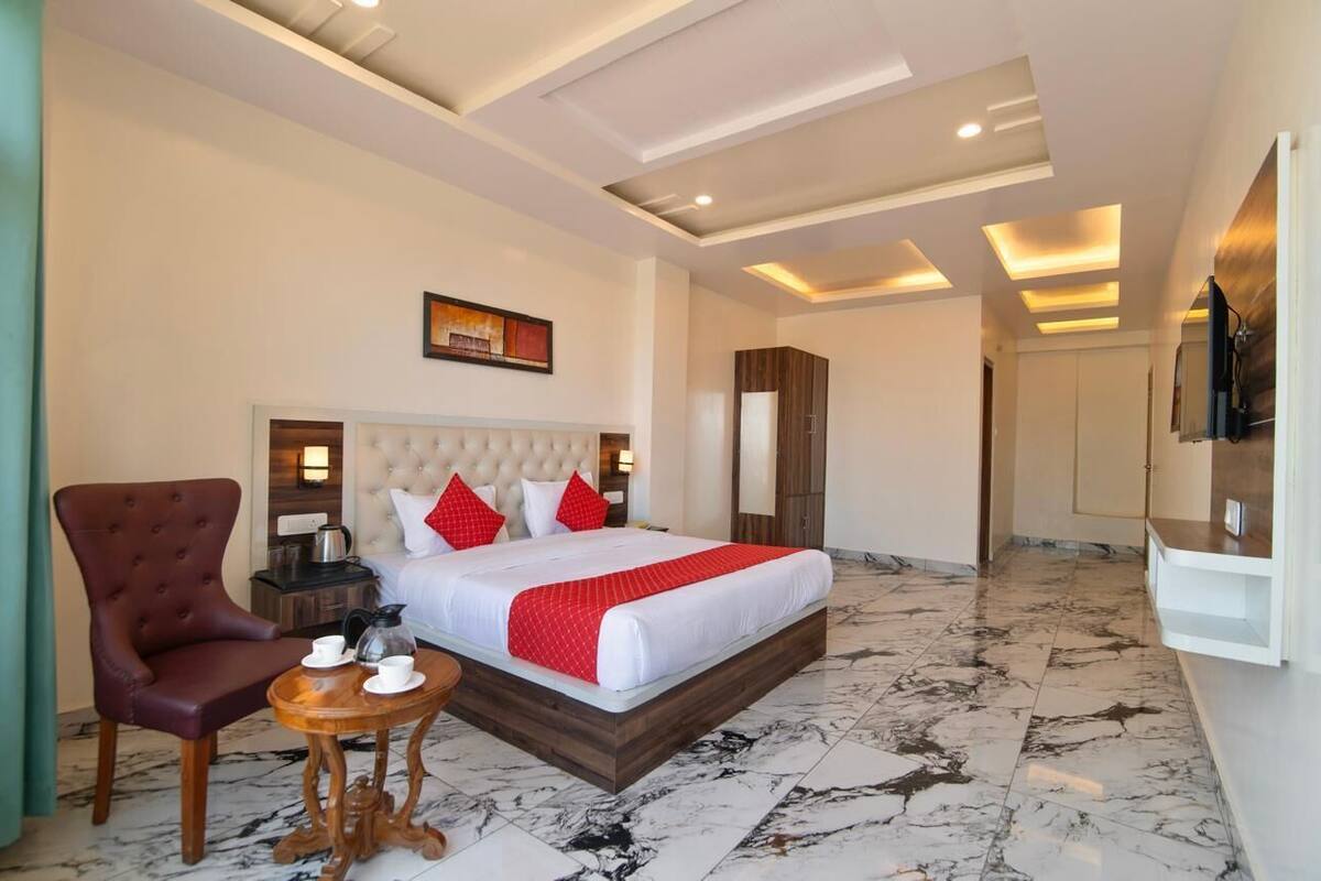 A hotel room with a large bed, a wooden chair, a small table with a coffee pot, and a TV on the wall.