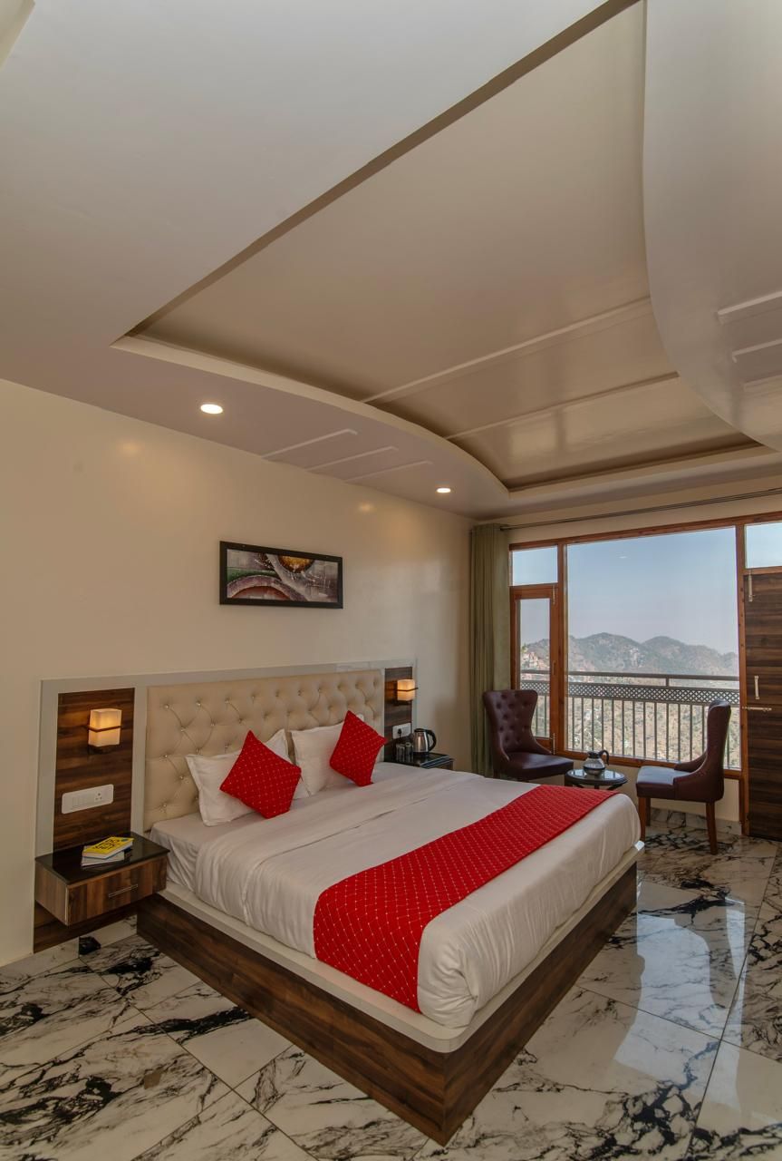 A hotel room with a large bed, a nightstand, a chair, a table, and a view of the mountains.