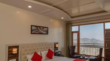 A hotel room with a large bed, a nightstand, a chair, a table, and a view of the mountains.