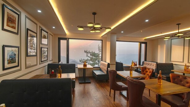 A modern restaurant with wooden tables and black cushioned seating, framed artwork on the walls, and large windows offering a view of the outdoors. - Shimla Inn (Shimla)