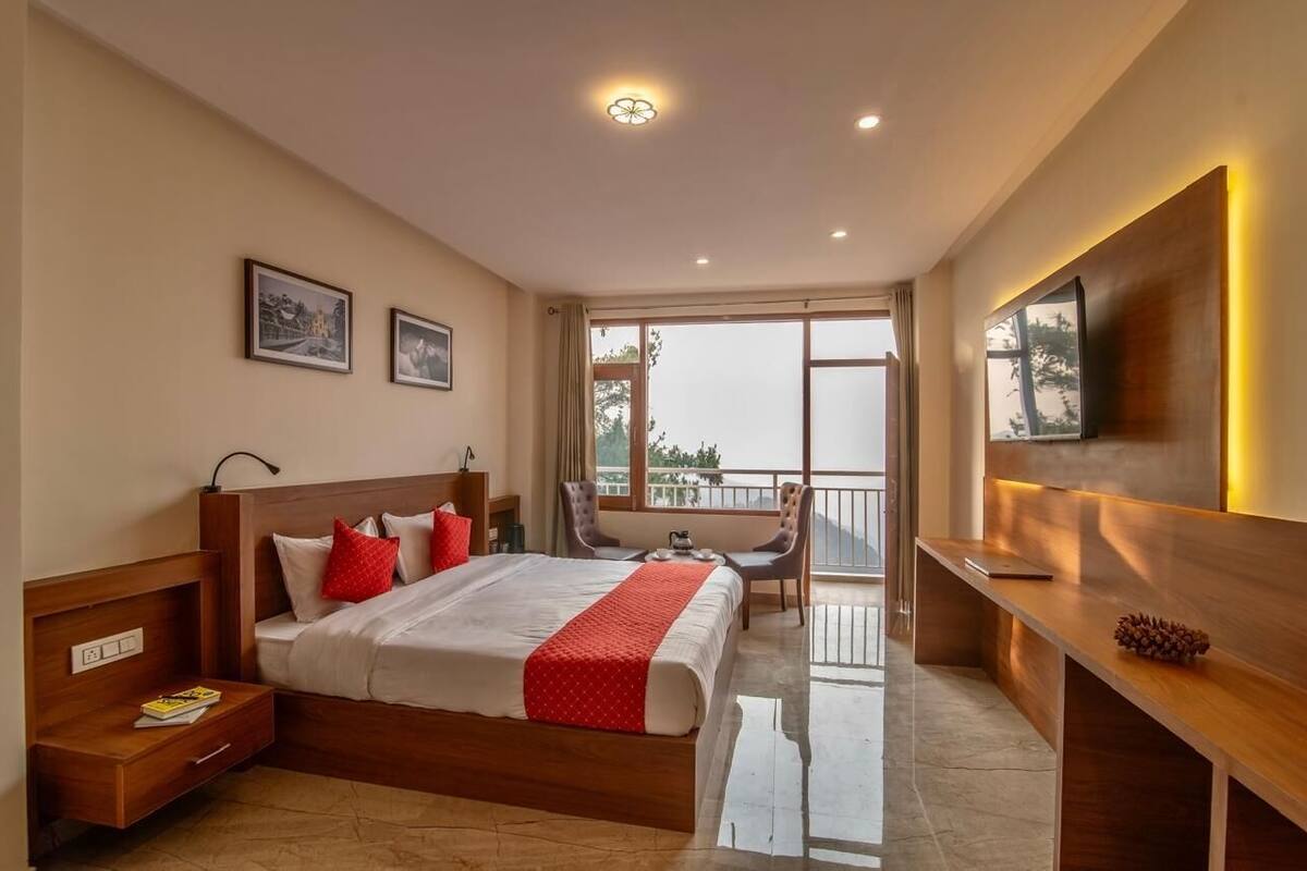A hotel room with a large bed, a desk, a chair, a TV, and a balcony with a view.