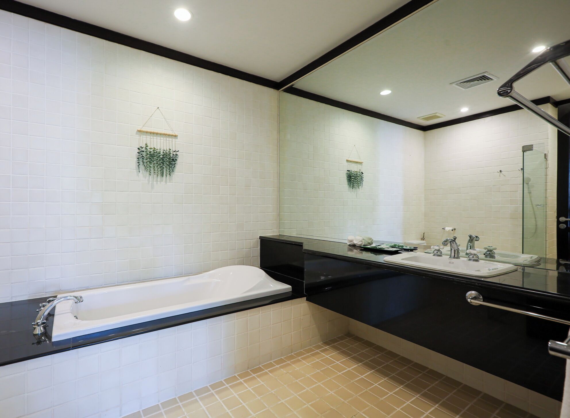 Ein modernes Badezimmer mit weiß gefliesten Wänden, einer schwarzen Arbeitsplatte, einer weißen Badewanne und einem großen Spiegel.