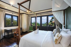 A bedroom with a large bed, a desk, and a chair. There are multiple windows providing a view of the outdoors.