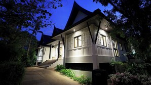 A two-story house with a steeply pitched roof, a front porch, and a well-lit exterior. - Katamanda villa Eden Large Villa near Kata Beach (Karon)