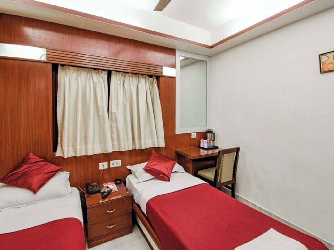 A hotel room with two beds, wooden headboards, a desk, and a chair.