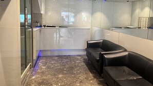 A modern waiting area with a glass partition, a reception desk, and a seating area with leather chairs. - Hotel Aston  (Kolkata)