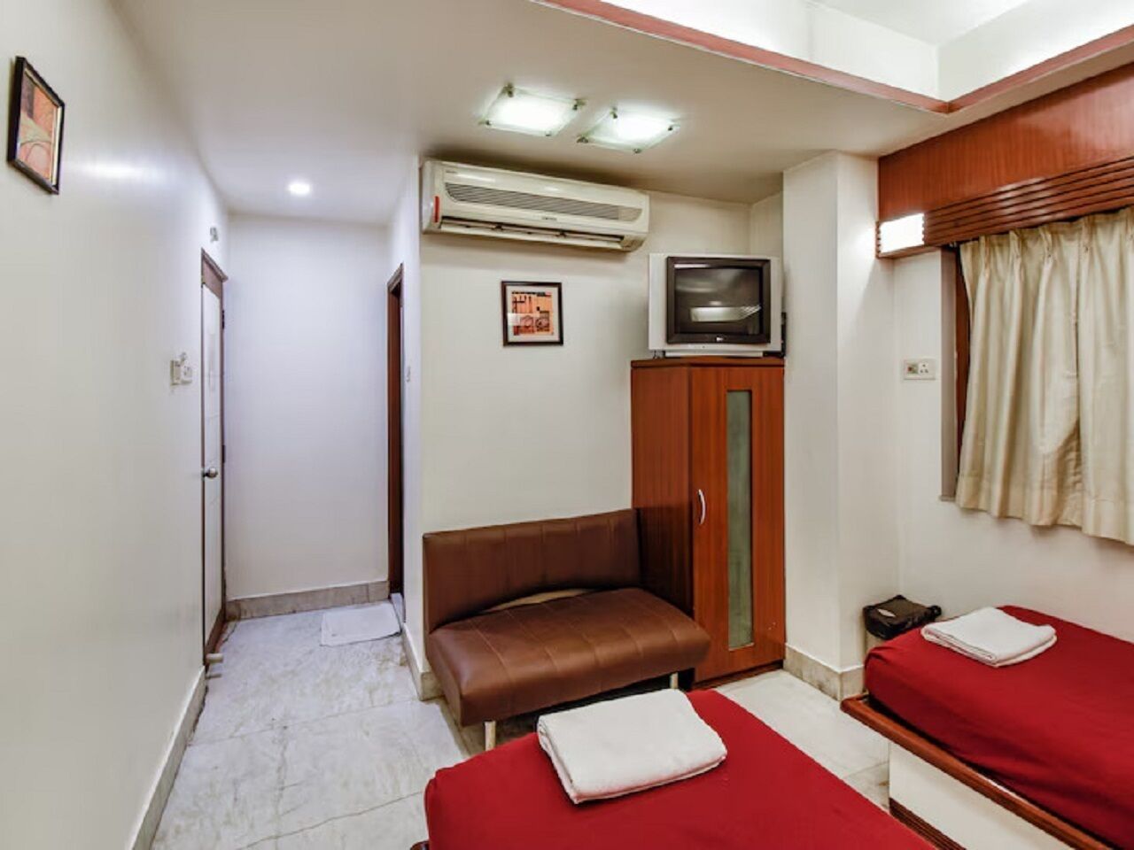 A compact hotel room with a single bed, a sofa, an air conditioning unit, a television, and a wardrobe.