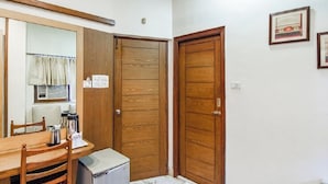 A compact room with a wooden dining table, chairs, a small refrigerator, and two wooden doors. - Hotel Aston  (Kolkata)