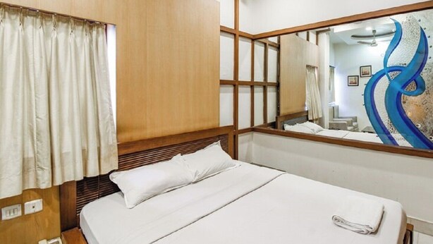 A hotel room with a bed, a wooden headboard, a mirror, and a window with curtains. - Hotel Aston  (Kolkata)