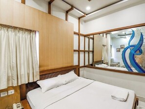 A hotel room with a bed, a wooden headboard, a mirror, and a window with curtains. - Hotel Aston  (Kolkata)