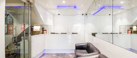 A reception area with a glass door, a reception desk, a seating area with leather chairs, and a large mirror reflecting the interior.