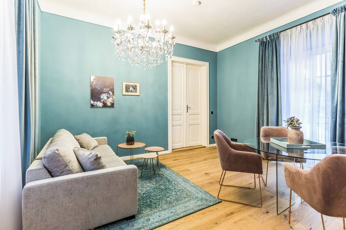 Una sala de estar moderna con un sofá, dos sillones, una mesa de vidrio y una araña.