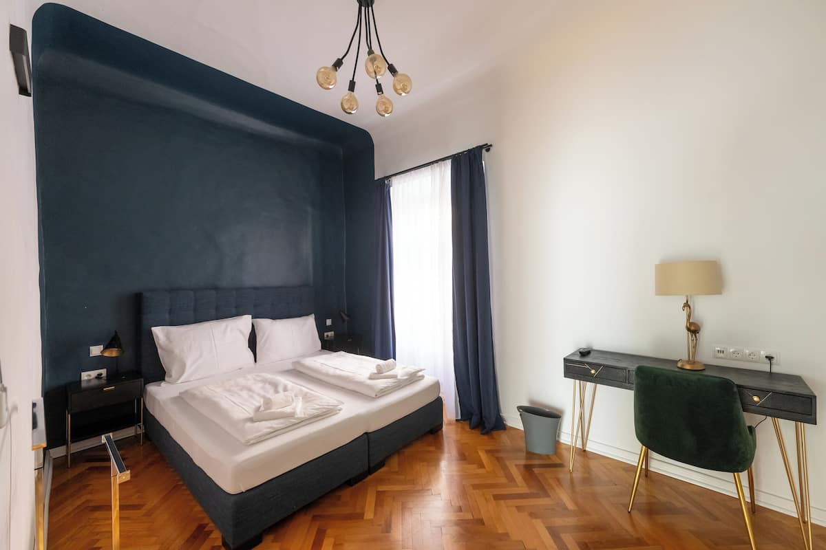 Un dormitorio con cama, escritorio, silla, lámpara y ventana con cortinas.