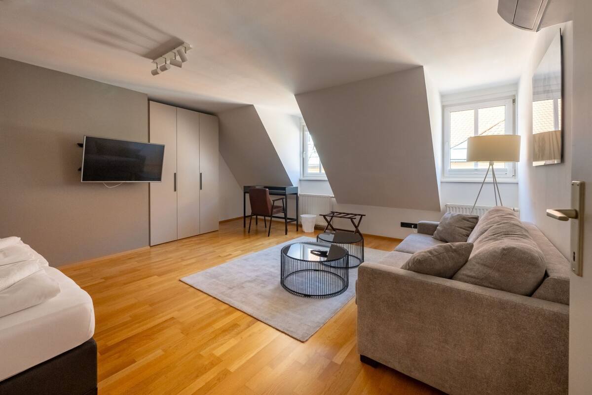 Un loft moderno con piso de madera, un sofá gris, un televisor y un comedor con mesa y sillas.