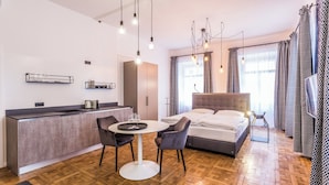 A modern hotel room with a kitchenette, a dining area, and a large bed.