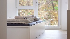 Een bed met een wit frame en uitzicht op bomen door een raam.